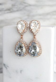 two tear shaped earrings on top of a white marble block with gold trimmings