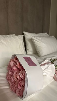 a bouquet of pink roses in a white paper bag on a bed with pillows and sheets