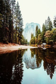 a mountain is reflected in the still water of a lake surrounded by trees and rocks