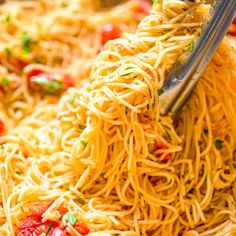 someone is using a fork to stir spaghetti in a bowl with tomatoes and parsley