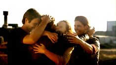 two men and a woman hugging each other in front of a building with the sun shining on them