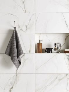 a white marble tile wall with shelves and towels hanging on the hooks in front of it