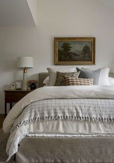 a bed with white linens and pillows in a bedroom next to a painting on the wall