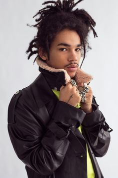 a young man with dreadlocks wearing a black jacket and holding a teddy bear