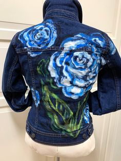 a woman's jean jacket with blue roses painted on the front and back of it