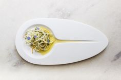 a white plate topped with pasta and sauce on top of a marble countertop next to a plastic spatula