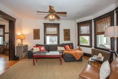 a living room filled with furniture and windows next to a wall mounted ceiling fan on top of a hard wood floor