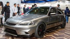 a silver car is on display at an auto show with people standing around and looking at it