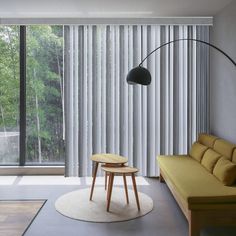 a living room filled with furniture and a large window covered in vertical blindes next to a wooden table