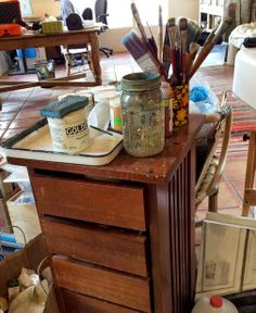 a wooden table topped with lots of different types of paint and brushes on top of it