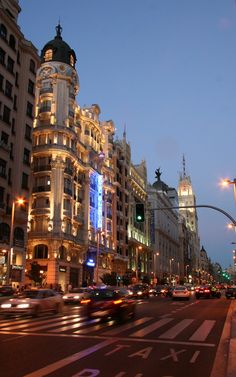 a city street filled with lots of tall buildings and cars driving down the road at night