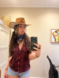 a woman taking a selfie with her cell phone wearing a cowboy hat and scarf