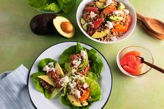 two white plates filled with lettuce, tomatoes and other food on top of a green table