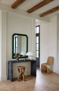 a room with a table, mirror and two chairs in front of the door that leads to another room