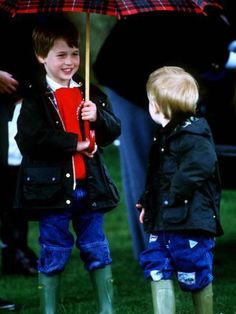 two young boys standing under an umbrella in the rain, one holding a red book