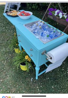 a blue cooler sitting on top of a grass covered field next to a bowl of fruit