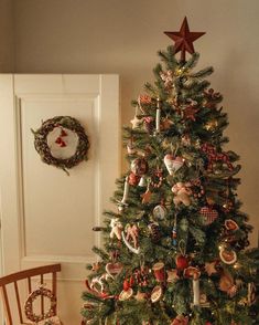 a decorated christmas tree in a living room next to a chair and wreath on the wall