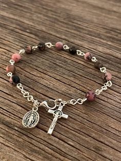 Beautifully made Rhodonite Rosary bracelet! Beads are 6mm Rhodonite Natural Stone, Crucifix is a 7/8" silver finished St. Benedict cross. Bracelet includes a mini 1/2" Silver Finish Miraculous Mary Medal.  Each one of my rosary bracelets starts its life as a spool of wire and a handful of beads. It is carefully assembled one link at a time so no two are ever exactly alike. A truly one-of-a-kind gift for your one-of-a-kind someone! They are sturdy enough to withstand the test of time, and sentimental enough to pass down for generations to come! **Size options**   1.  5 1/2" Baby-age 3   2.  6" - age 4-7   3.  6 1/2" - age 8-11   4.  7" - age 12- Women Petite   5.  7 1/2" - Women Average   6.  8" - Women Large   7.  Custom Size If 'Custom Size' is needed please specify at checkout (recipient Cheap Adjustable Metal Rosary Bracelet, Cheap Elegant Rosary Bracelet, Rosary Bracelet Catholic, Catholic Rosary Bracelet, St Benedict Cross, Catholic Bracelet, Bead Rosary, St Benedict, Rosary Bracelet