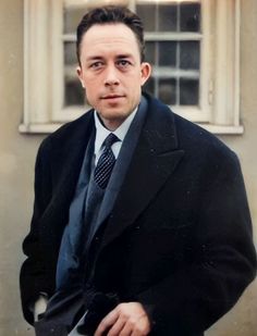 a man in a suit and tie standing next to a building with a window behind him