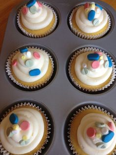 cupcakes with white frosting and colorful decorations in a muffin tin on a wooden table