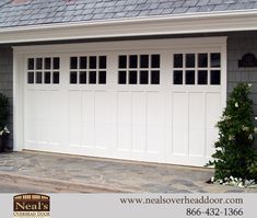 a white garage door with windows on the side of it and two bushes in front