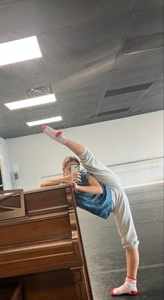 a young boy doing a hand stand on top of a piano in an empty room