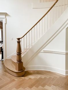 a white staircase with wooden handrails next to a wood flooring area in a house