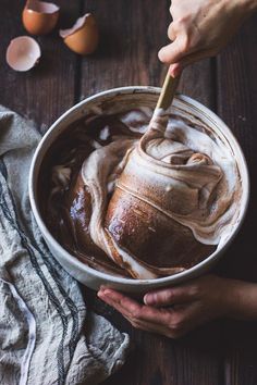 two hands holding a spoon over a bowl filled with chocolate and marshmallows