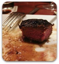 a piece of steak sitting on top of a white plate next to a fork and knife