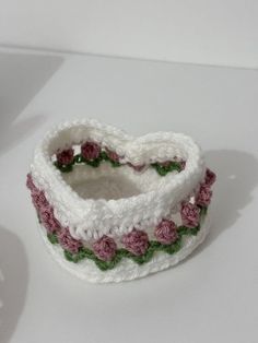 a crocheted white and pink bracelet with flowers on the side, sitting on a table