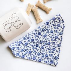 a dog bandana next to some treats on a white table with blue and white flowers