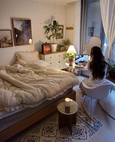 a woman sitting on a chair in front of a bed with white sheets and pillows