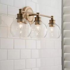 three light bathroom fixture with clear glass globes on the wall and white tiled walls