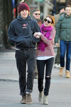 a young man and woman walking down the street holding hands while wearing winter clothes,