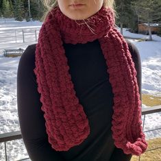 a woman standing in the snow wearing a red crocheted scarf and black top