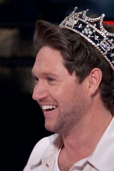 a man with a crown on his head smiles at the camera while wearing a white shirt