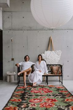 a man and woman sitting on a bench in front of a rug