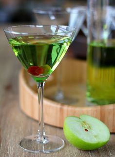 an apple sits next to a martini glass on a wooden tray with green liquid in it