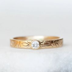 a yellow gold ring with a diamond on the top, sitting on a white surface