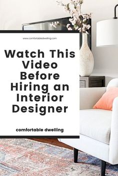 a living room with a white chair and black framed sign that says watch this video before hiring an interior designer