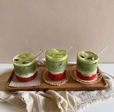 two cups with strawberries in them sitting on a wooden tray next to another cup