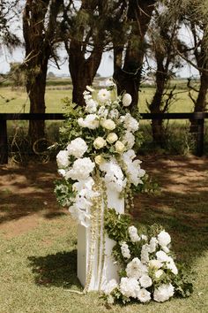 a tall white flower arrangement sitting on top of a grass covered field next to trees