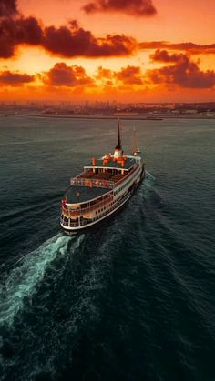 a large boat traveling through the ocean at sunset or sunrise with clouds in the sky