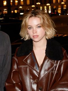 a woman in a brown leather jacket is looking at the camera