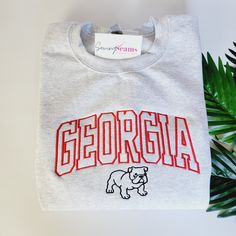 Experience the perfect blend of style and school spirit with our Georgia Bulldog Crewneck Sweatshirt or T-shirt! Available in three colors, this sweatshirt is designed to keep you cozy and comfortable, whether you're cheering in the stands or just showing off your Bulldog pride around town. At the heart of its design is the iconic "Georgia" embroidery, boldly presented across the center chest. The word is intricately stitched in a vibrant red, capturing the essence of the University of Georgia's Georgia Bulldog Shirts Women, Georgia Embroidery, Georgia Hoodie, Georgia Sweatshirt, Cheer Tops, Georgia Bulldogs Shirt, Uga Football, Personalized Slippers, Georgia College