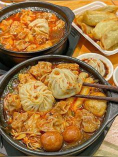 two pans filled with dumplings and vegetables on a table next to plates of food