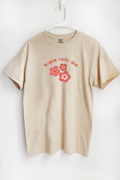 a white t - shirt with pink flowers on it hanging from a hanger against a wall