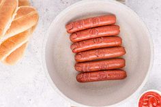 four hot dogs in a bowl next to bread and ketchup