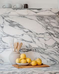 some lemons are sitting on a cutting board in front of a marble counter top