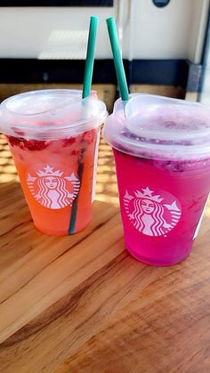 two starbucks drinks sitting on top of a wooden table next to each other with straws in them